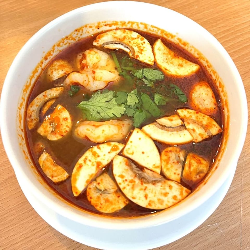 Spicy Tom Yum soup with shrimp, mushrooms, and cilantro in a white bowl on a wooden table.
